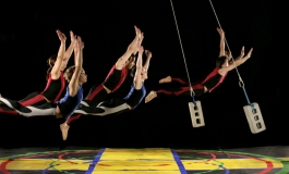 Five dancers seem to fly several feet off a colorful stage floor while two cinderblocks suspended on wires swing among them. 