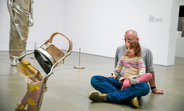 A child sits in her parent's lap on the floor of a gallery, looking at artwork