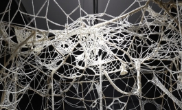 An installation of crocheted, off-white yarn covers the walls and ceiling of a small dark room.