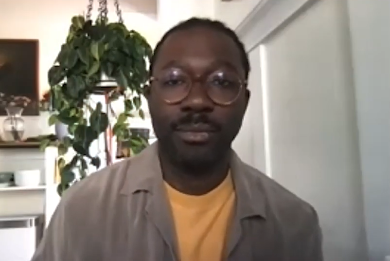 portrait of artist Paul Sepuya who has dark skin and is wearing a yellow shirt with a beige shirt over it and glasses