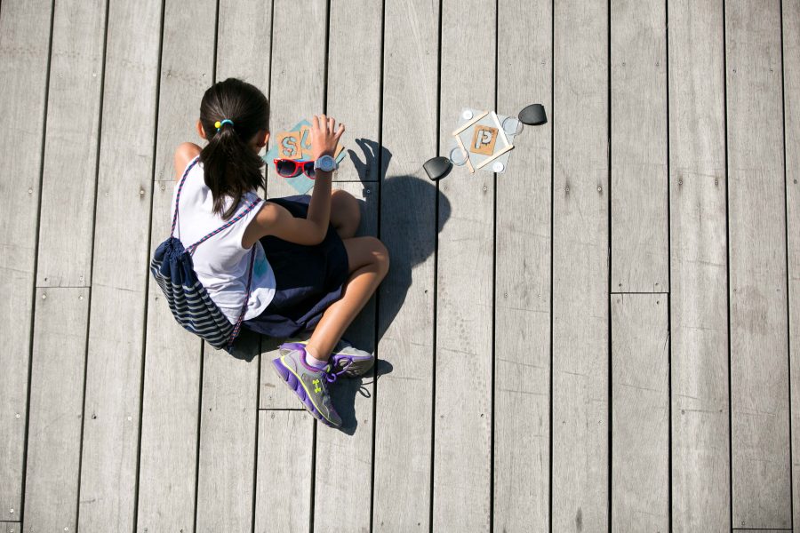 An elevated shot of a young child sitting on a wooden deck with art supplies