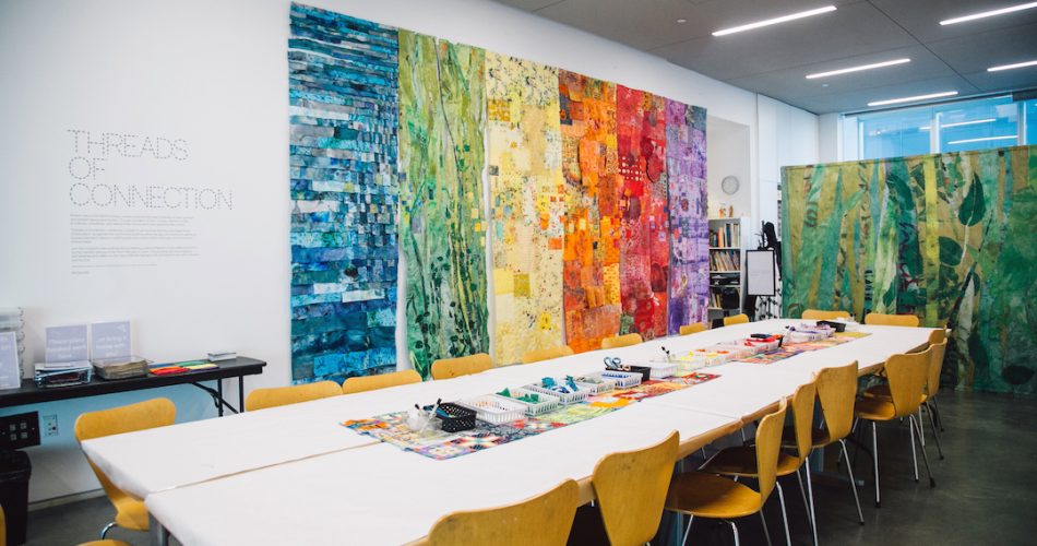 Large colorful wall panels and a long table with a white covering and art materials in the Bank of America Art Lab