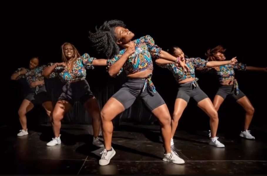 A group of Black female dancers wearing matching patterned tops and black shorts dancing