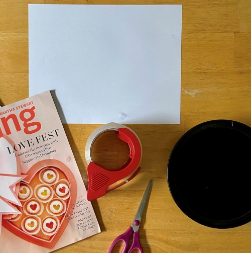 Art materials including clear packing tape, scissors, glossy magazine, white sheet of paper, and a black plastic bowl.