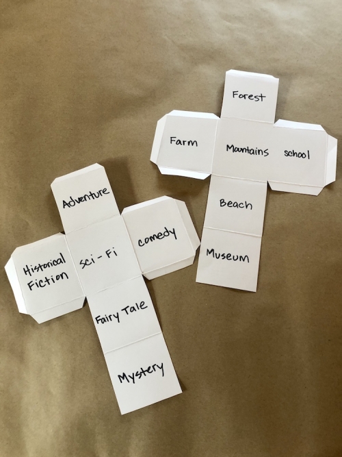 Two cut-out dice with writings of genres and settings on each side.