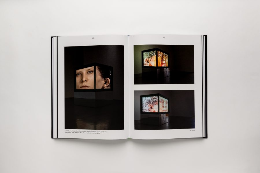 A book spread with large color photos of a video installation that is presented on sides of a large box in a dark room