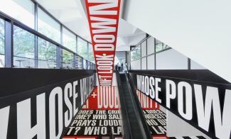 Installation utilizing white text on red and black backgrounds surrounding escalator