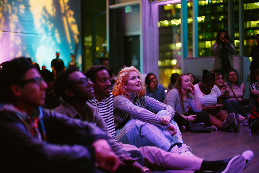 Visitors sit on the floor, watching a performance. 