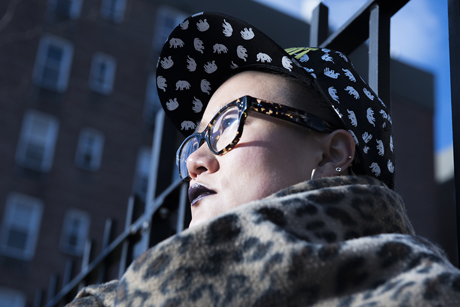 Diana Oh standing outside wearing glasses, a leopard print scarf, and a hat with elephants. 