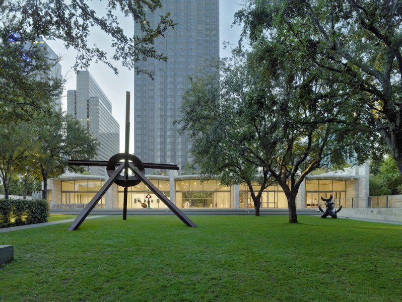 Two Modernist sculptures erected over the lawn and greenery in front of the building facade of the Nasher Sculpture Center.