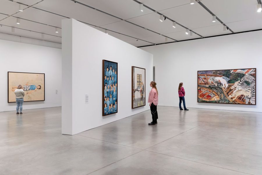 A gallery with three people looking at large colorful paintings