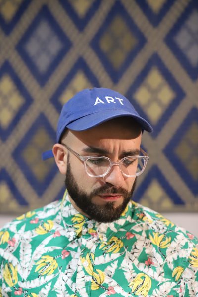 Anthony Febo wearing a cap that says ART and sitting in front of a diamond-patterned wall. 