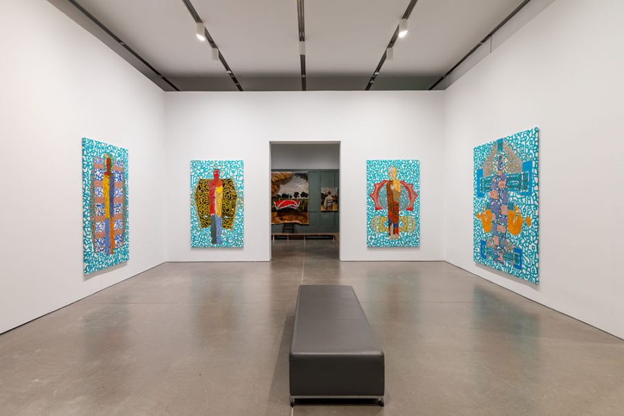 A gallery with four of Marlon Forrester's paintings hanging and the next exhibition in view through the doorway. The paintings all have a multi-colored figure against a teal and white pattern.