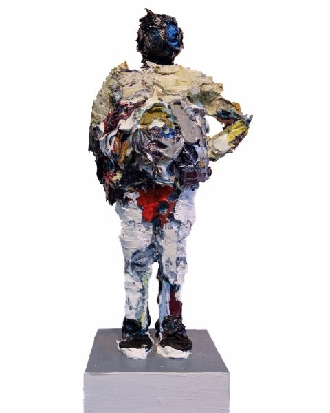 A standing figure that appears to be sculpted from thickly applied oil paint of different colors stands with one hand on his hip, on a small square base.