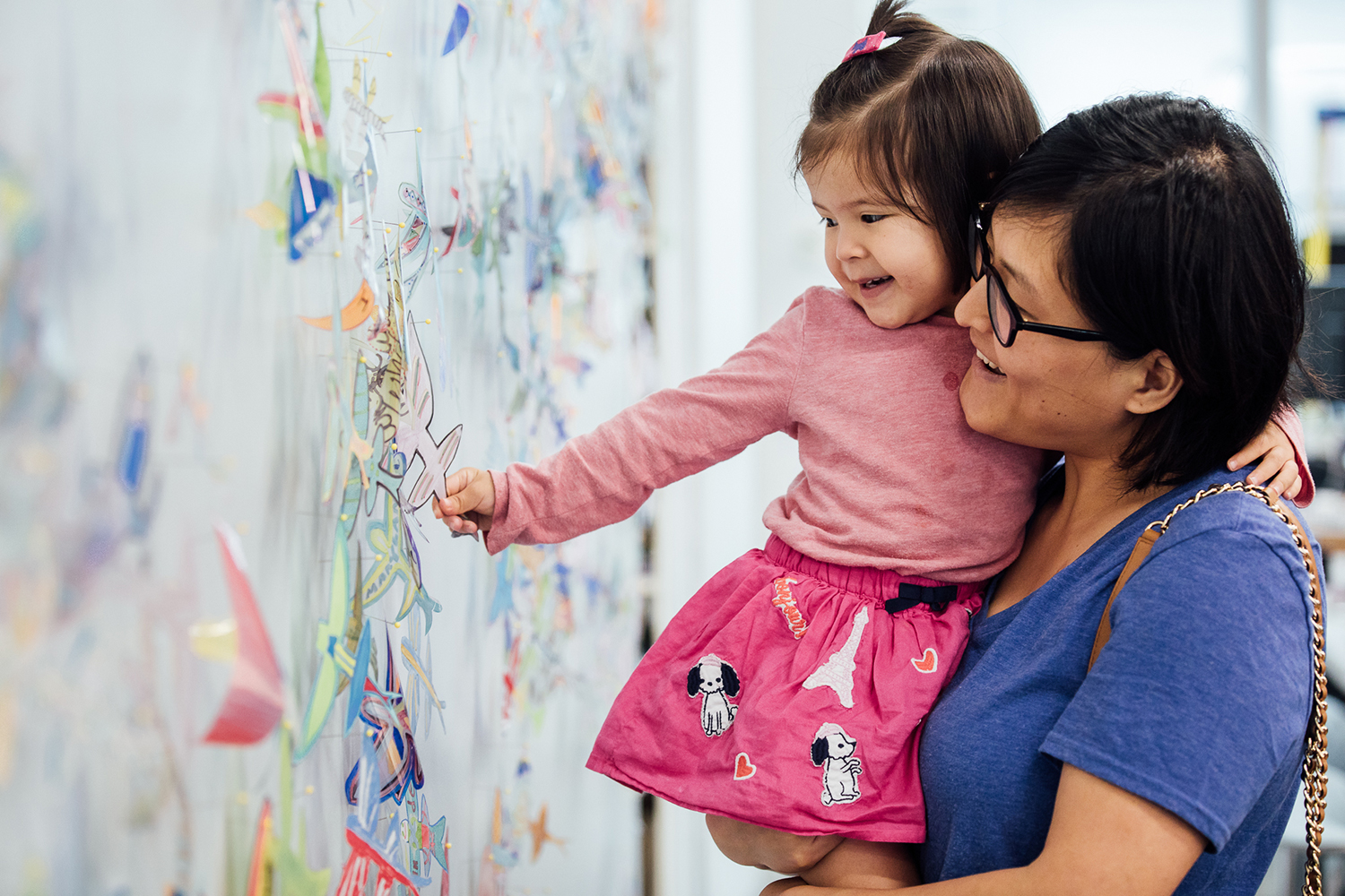 A parent holds their child as they examine interactive artwork