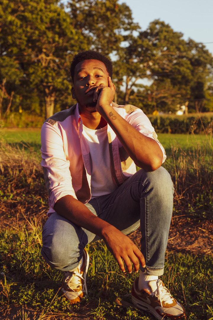 A young African-American man in a casual kneeling pose in a park with glowing and natural dusk lighting.