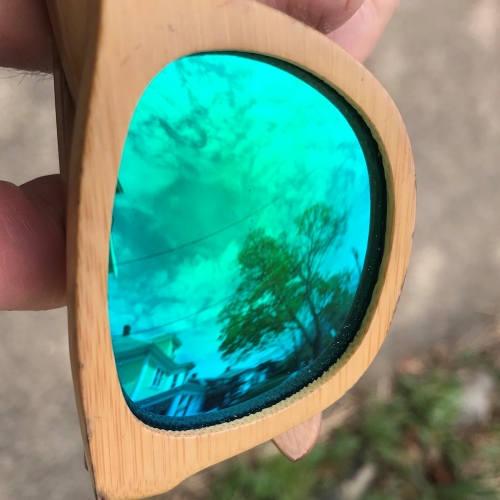A close-up, sideway view of one lens of a green-tinted sunglasses with wood frames.