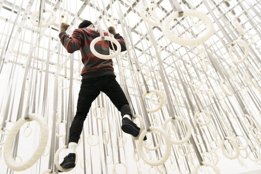 A young man climbs among hundreds of gymnastic rings suspended from the ceiling.