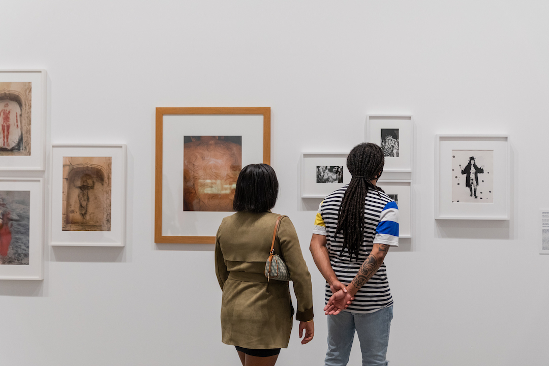 Two visitors from behind viewing framed photographs on the gallery wall.