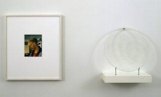 An installation of two objects hung side by side a framed reproduction of Sandro Botticelli's "Virgin and Child with an Angel" oil painting and a circular glass plate speckled in gold stars that casts a halo shadow on the wall.