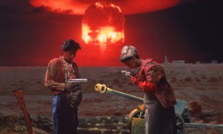 A color photograph depicts a scene of two Asian peasants, one played by the artist, posing with weapons in an open, devastated field as a red nuclear mushroom cloud blooms in the horizon.