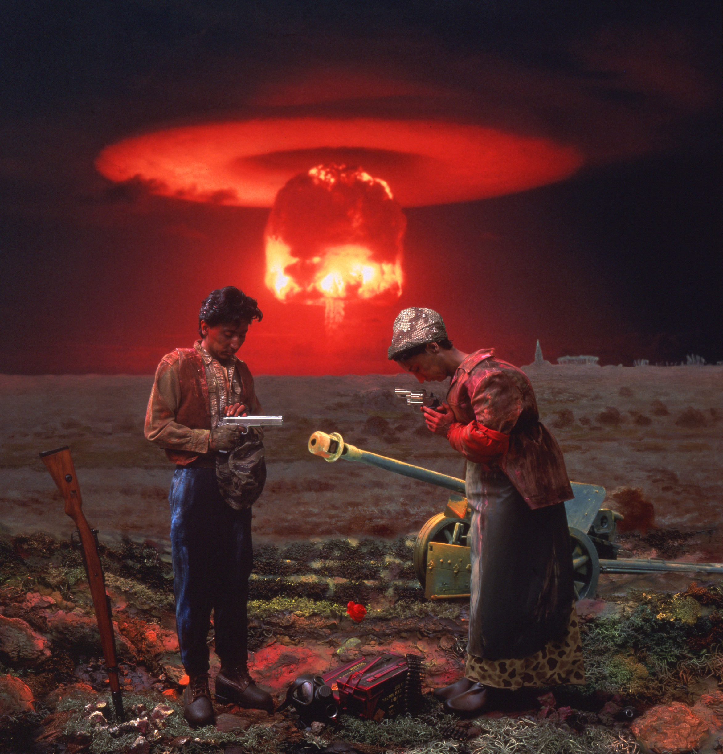 A color photograph depicts a scene of two Asian peasants, one played by the artist, posing with weapons in an open, devastated field as a red nuclear mushroom cloud blooms in the horizon.