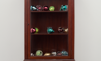 A sculpture comprising an Edwardian wooden cabinet filled with colorful Murano glass grenades that resemble decorative fruit.