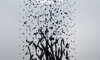 A suspended sculpture of charred, broken pieces of charcoal arranged densely at the bottom and sparsely at the top, as though rising from ashes.