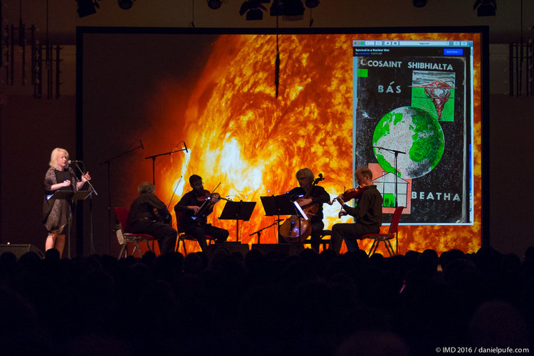 A seated string quartet and a standing person in front of a projected image of fire.