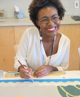 A headshot of Dyeemah Simmons sitting at a table and painting a landscape.
