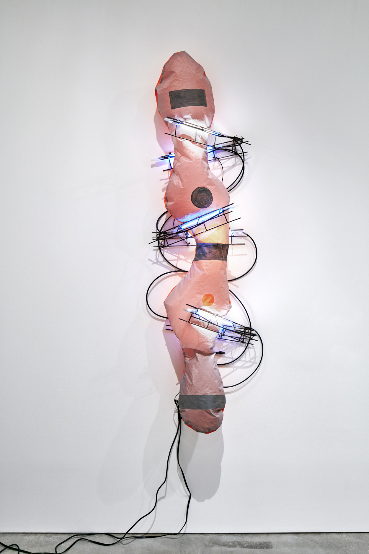 A wall sculpture composed of soft pink nylon, rebar, and lit neon lights and electrical cord.