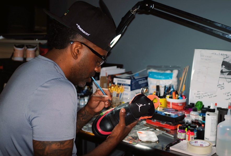 Guy painting Air Jordan sneaker surrounded by art supplies