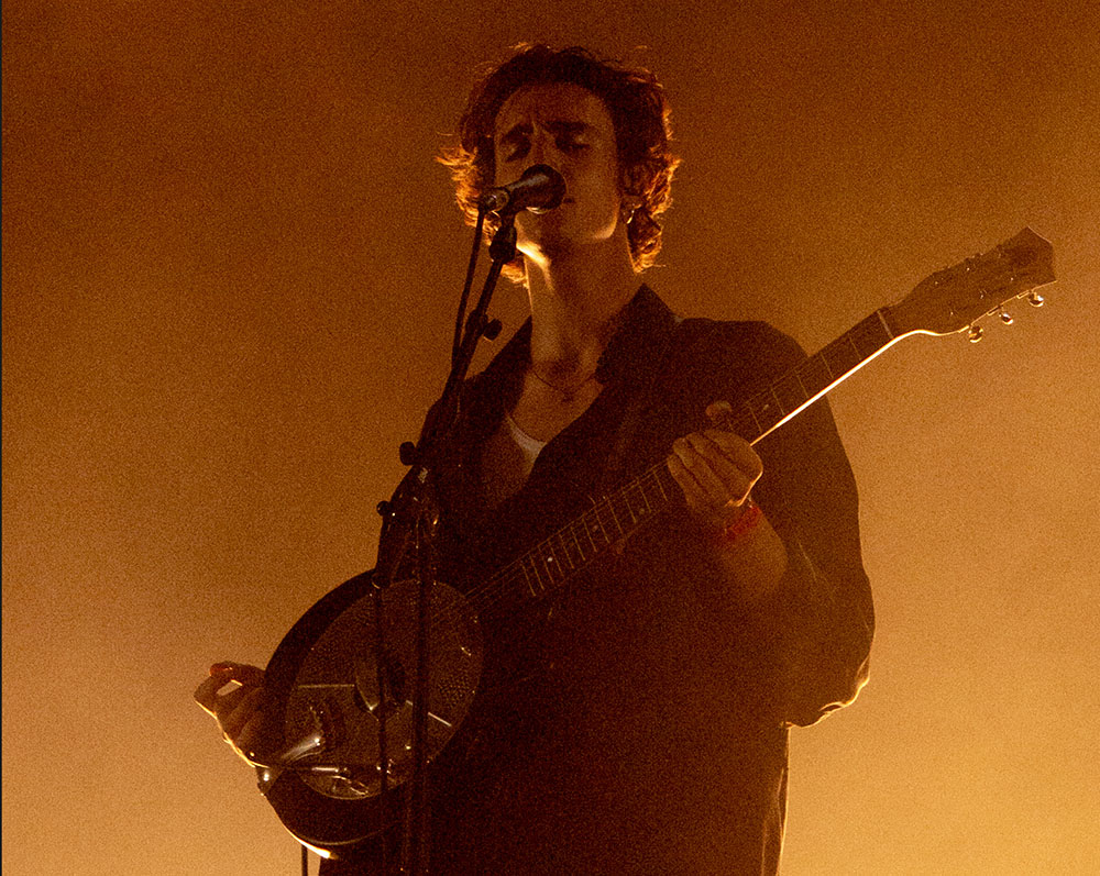 A sepia-toned image of Tamino playing guitar and singing into a microphone.