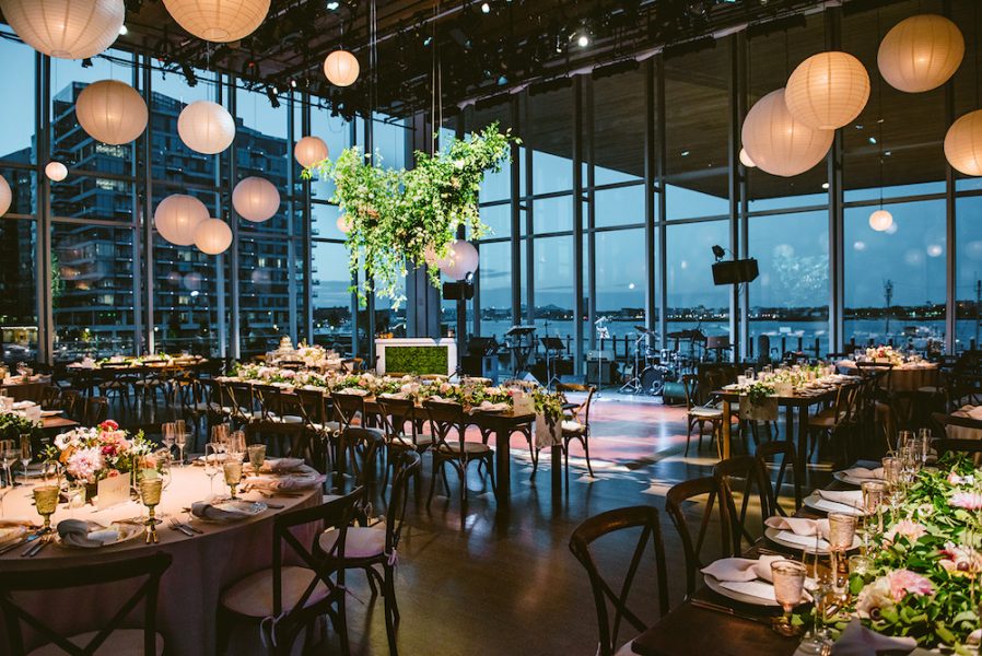 The ICA's theater is set for an event with wide views of Boston Harbor, low lighting, paper lanterns, and tables set for dinner.