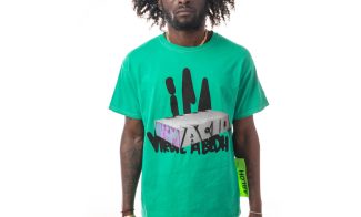 Front view of bright green shirt with graffitied white block slightly obscuring thick graffiti-like black text saying "ICA" and "Virgil Abloh", worn by a dark skinned model.