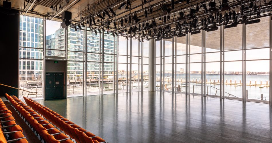 Photo of theatre with orange rows of seats and large glass windows overlooking Boston harbor