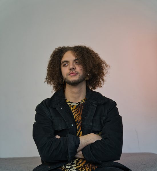 Person with a leather jacket and tiger print shirt crosses their arms