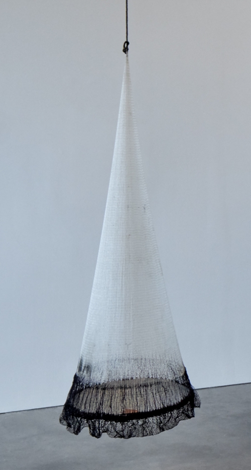 A conical hanging sculpture made from a fishing net that is white except for a dark bottom, the widest part.