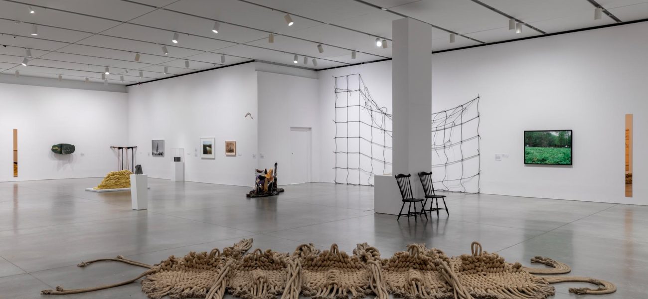 Wide gallery with works on walls and sculptural works, including large knit installation on floor