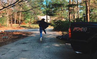 A young person jumping mid-air over an asphalt driveway in a rural neighborhood.