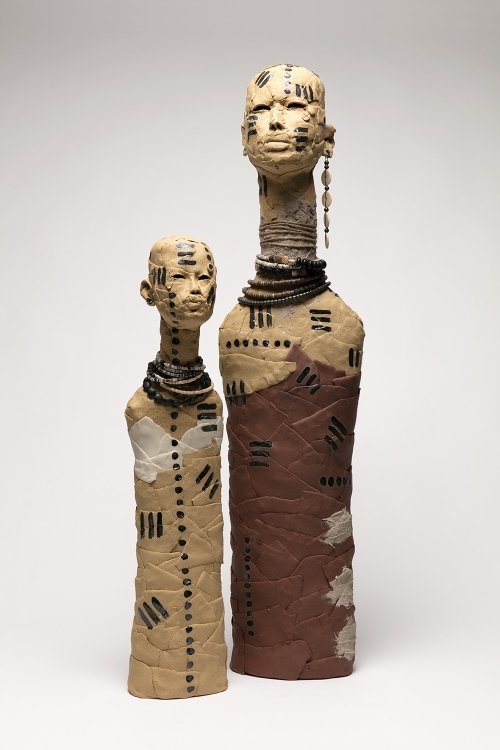 Two slender, clay armless busts with black striped or dotted markings