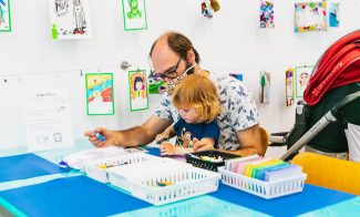 A parent and a young child work on creating art together at a table