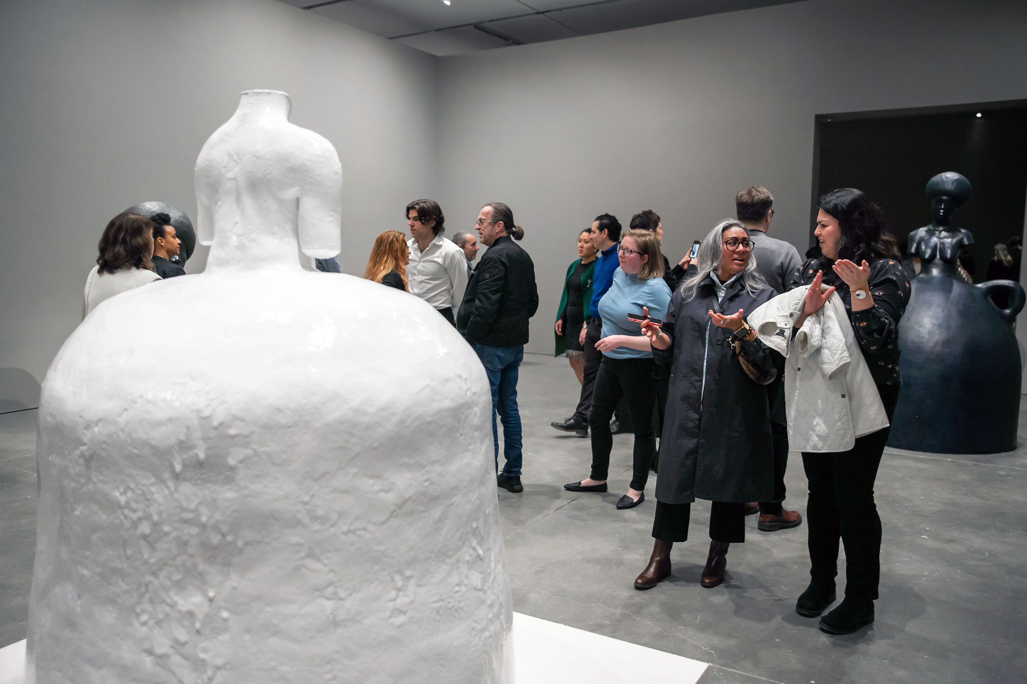 A group of people look and talk about a large white ceramic sculpture