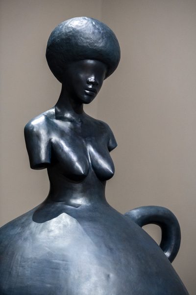 Metal sculpture of a woman with a jug handle and flared skirt