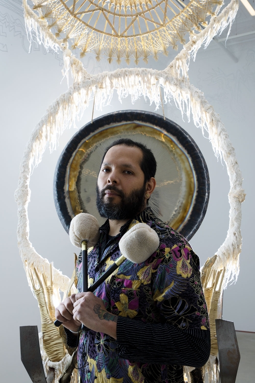 Artist Guadelupe Maravilla standing front of a gong sculpture holding two felted mallets 
