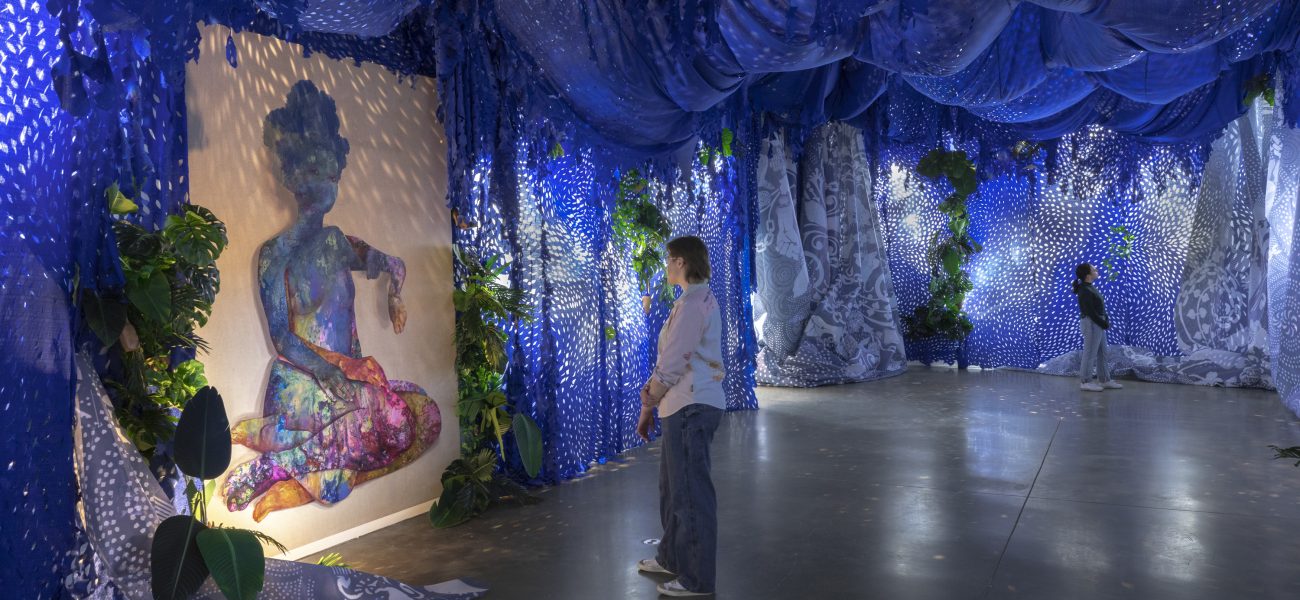 Room draped with bluue fabric and a hanging painting of a female figure