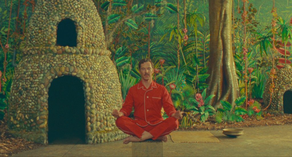 Benedict Cumberbatch in red pajamas sitting cross-legged in a staged jungle scene