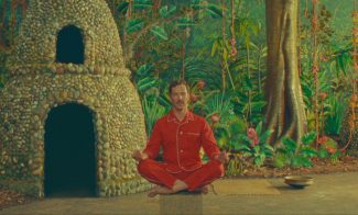 Benedict Cumberbatch in red pajamas sitting cross-legged in a staged jungle scene