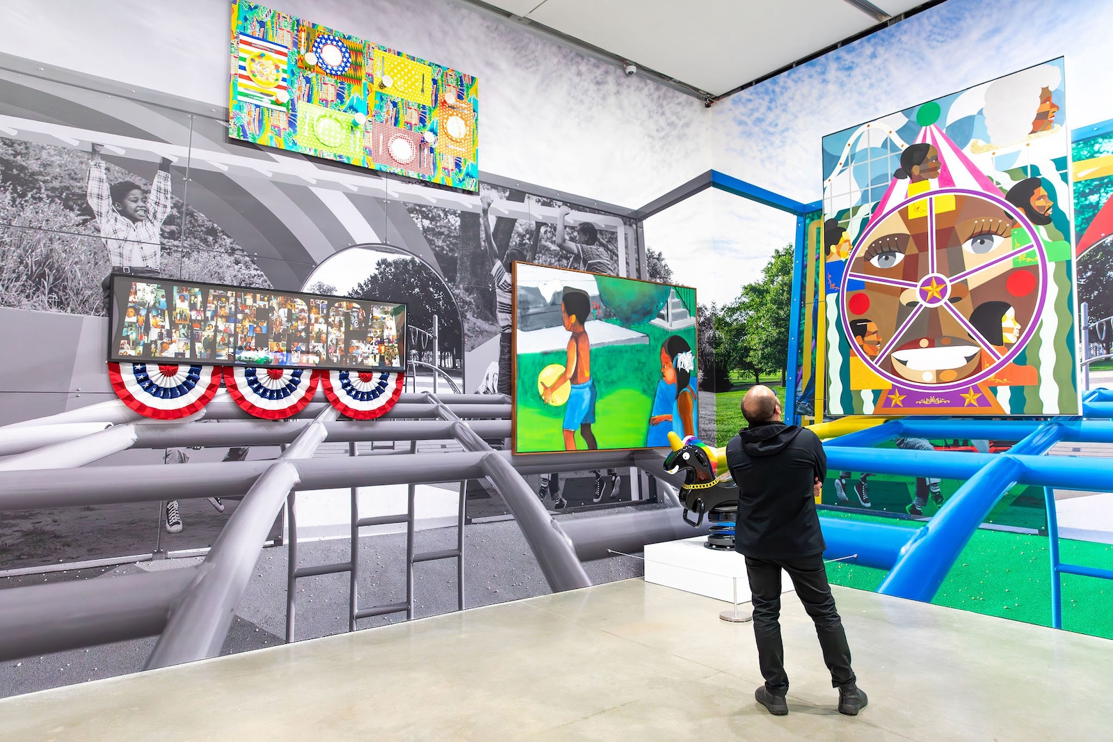 A person views colorful, large-scale artwork of children playing, layered over a black-and-white playground mural at an art gallery. Enjoy these vibrant paintings with august free admission at the ICA.