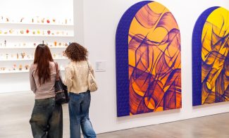 Two people with long hair walk past large, colorful abstract paintings with swirling purple and orange patterns at ICA Boston. Small sculptural pieces are displayed on shelves in the background during Martin Luther King Day.